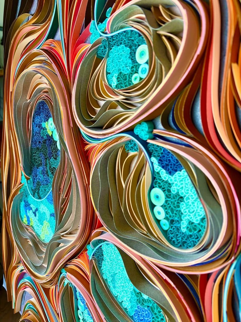 Close-up of layered paper ribbons in copper, tan and coral curling around pools of tiny cyan and teal paper coils